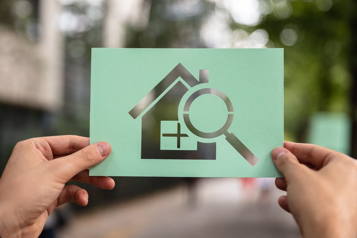 Hands Holding Paper With Cutout House And Loupe